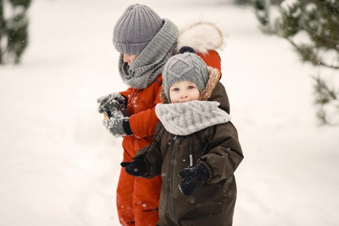 Kids in a knited hat. Little childrens plays with snow.
